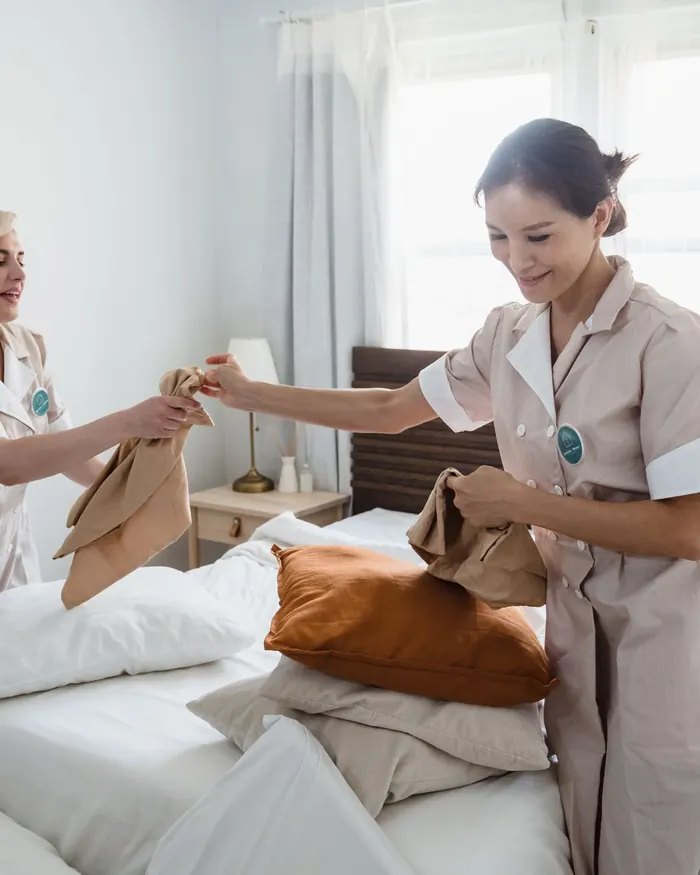 Housekeepers folding fresh linens in a bright bedroom