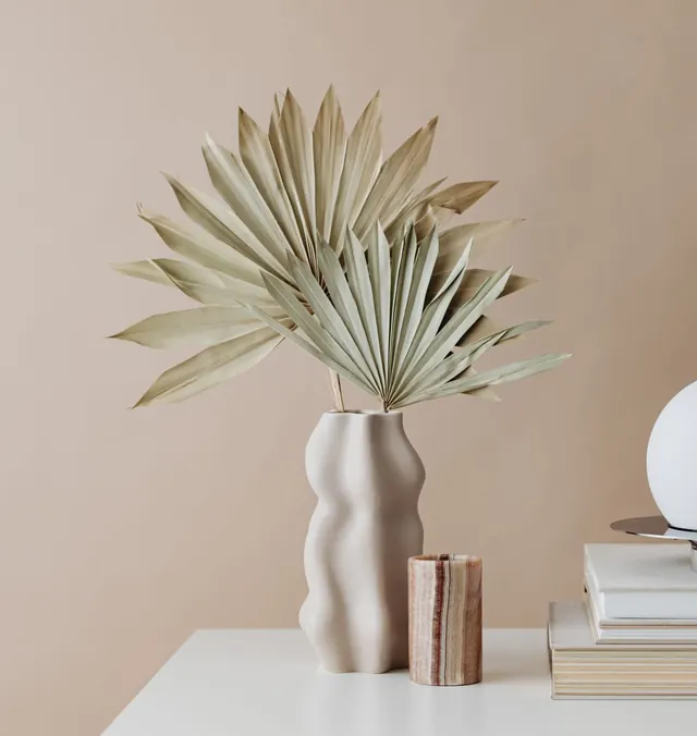 Ceramic vase with dried palm leaves on a white table against a warm beige wall