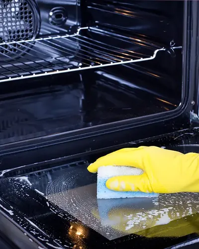 Gloved hand cleaning the inside of an oven door