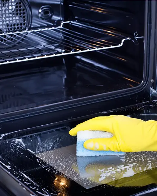 Gloved hand cleaning the inside of an oven door