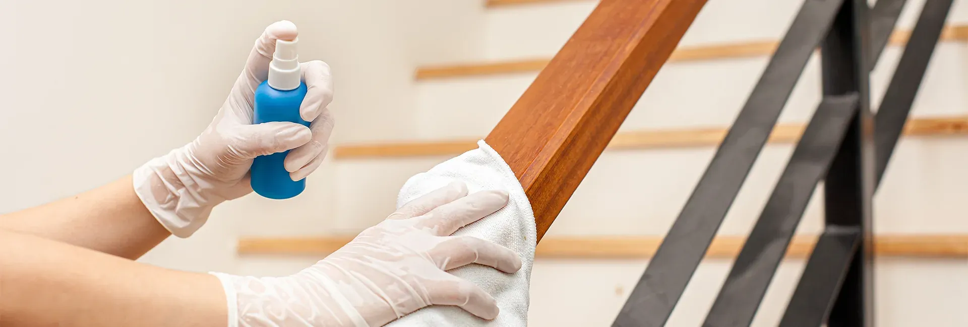 Gloved hands spraying and wiping a stair handrail